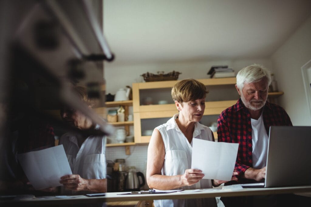 Should You Ditch That Old With-Profits Policy Before You Retire? 4 Midlife couple reviewing paperwork together at their kitchen table